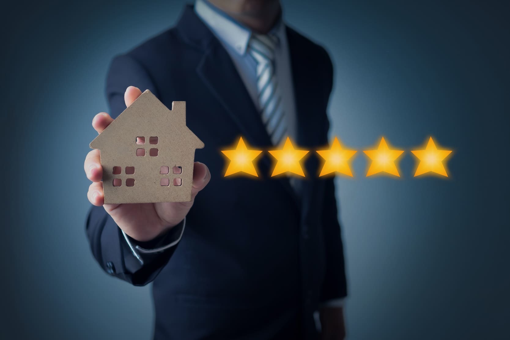 Man holding a model of a home next to five stars to represent excellent property management services.